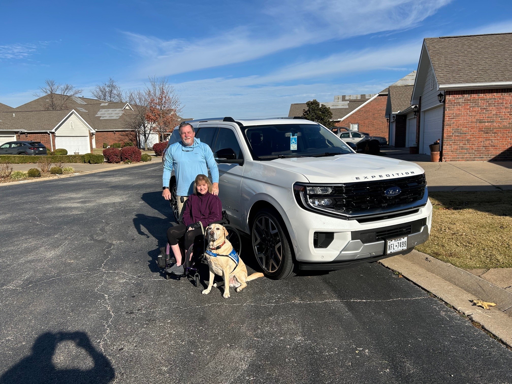 A man and his wife pose with their dog near a white truck.